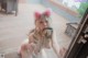 A woman in a pink cat ears is sitting on a wooden floor.
