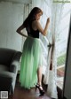 A woman standing in front of a window with a green skirt.