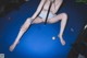 A naked woman sitting on a pool table holding a cue.