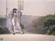 A woman in a white dress and hat walking down a street.