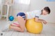 A woman in a white shirt and blue shorts is sitting on an exercise ball.