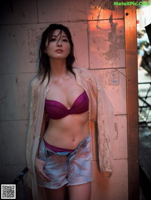 A woman in a purple bra top and denim shorts posing for a picture.